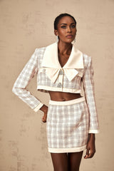 A pink tweed jacket and skirt set with a checkered pattern featuring a fitted blazer and matching mini skirt in a classic Chanel inspired style