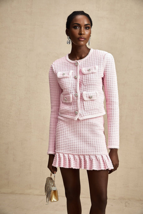 A pink waffle knit jacket and matching skirt set called Fabienne The outfit features a textured fabric in a soft pink color