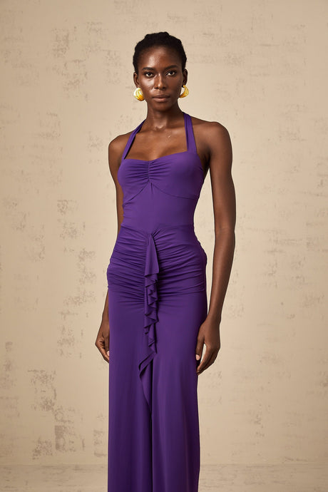 A purple halterneck midi dress with ruched detailing worn by a model standing against a plain background