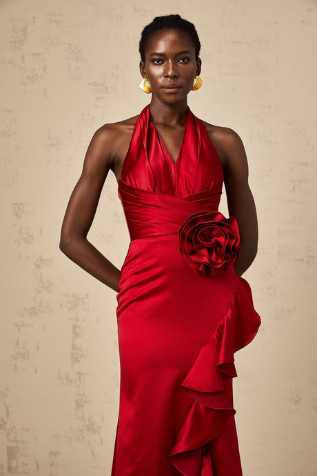 A red halterneck maxi dress with 3D petal ruffles adorning the bodice and skirt featuring a flowing silhouette and open back design