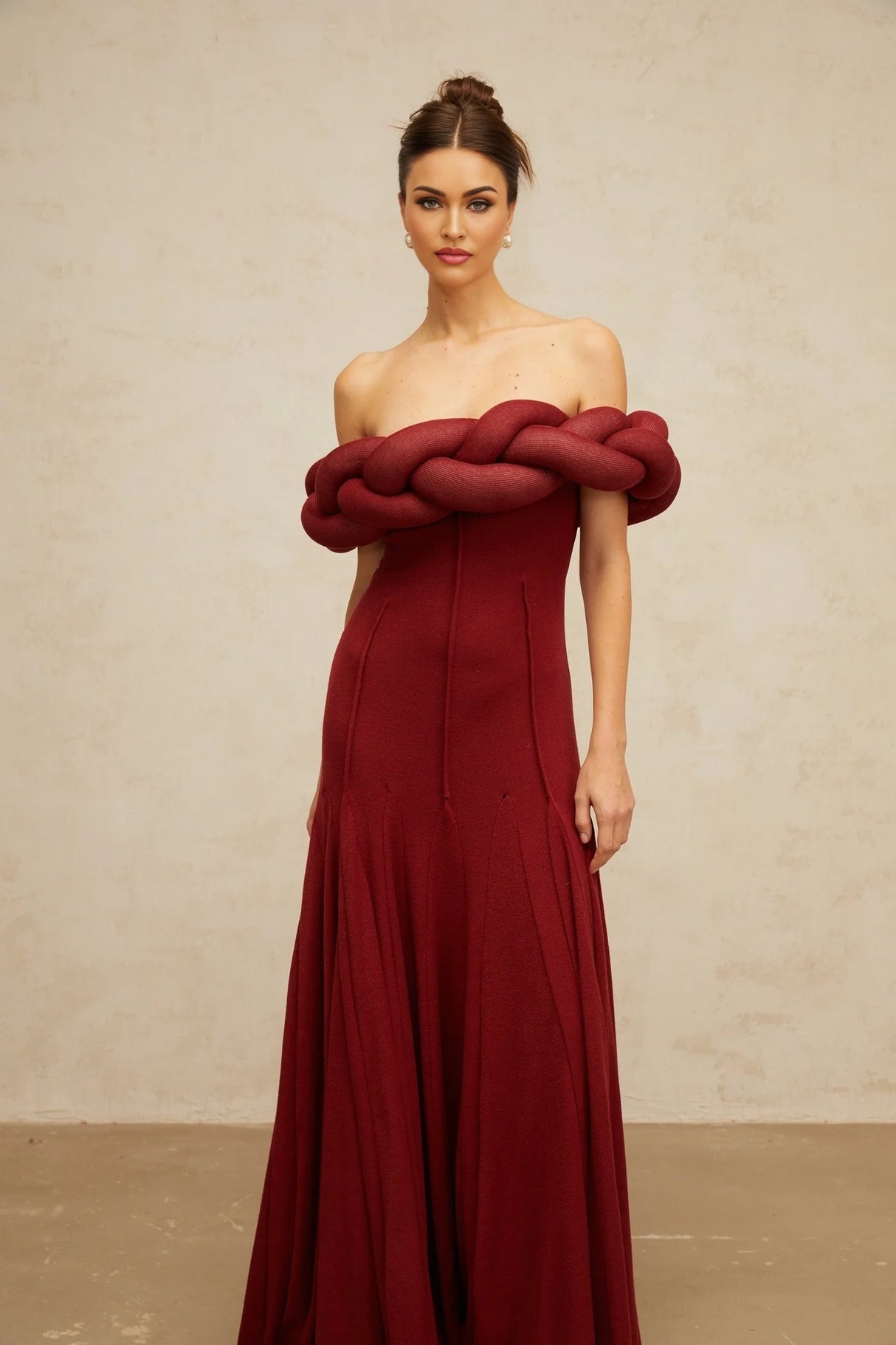 A red knit maxi dress with a braided design pattern worn by a model standing against a plain background
