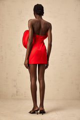 A red mini dress with an offshoulder neckline featuring a large sculptural rose detail positioned near the shoulder