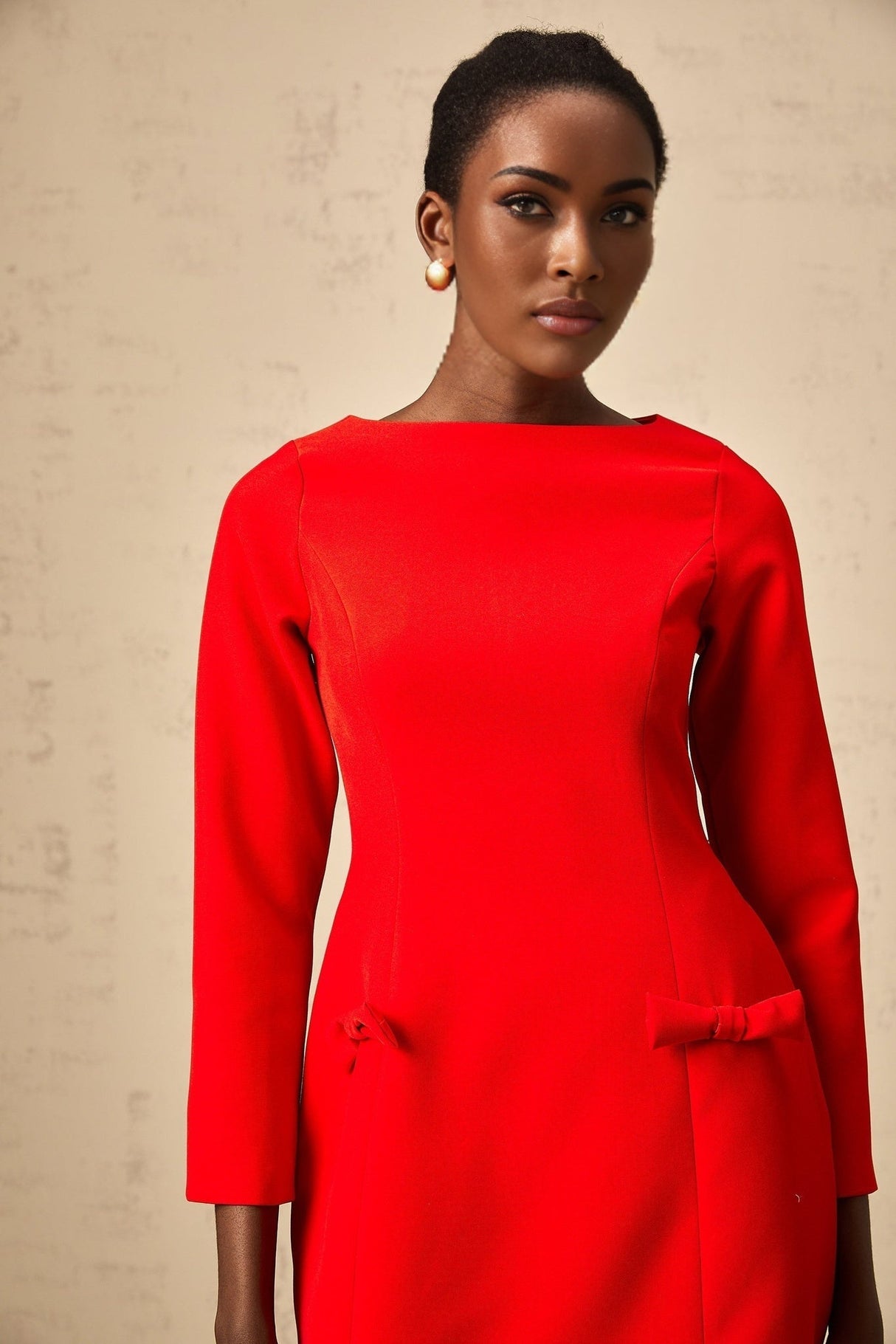 A red mini dress with long sleeves and a prominent bow detail at the neckline named Magali
