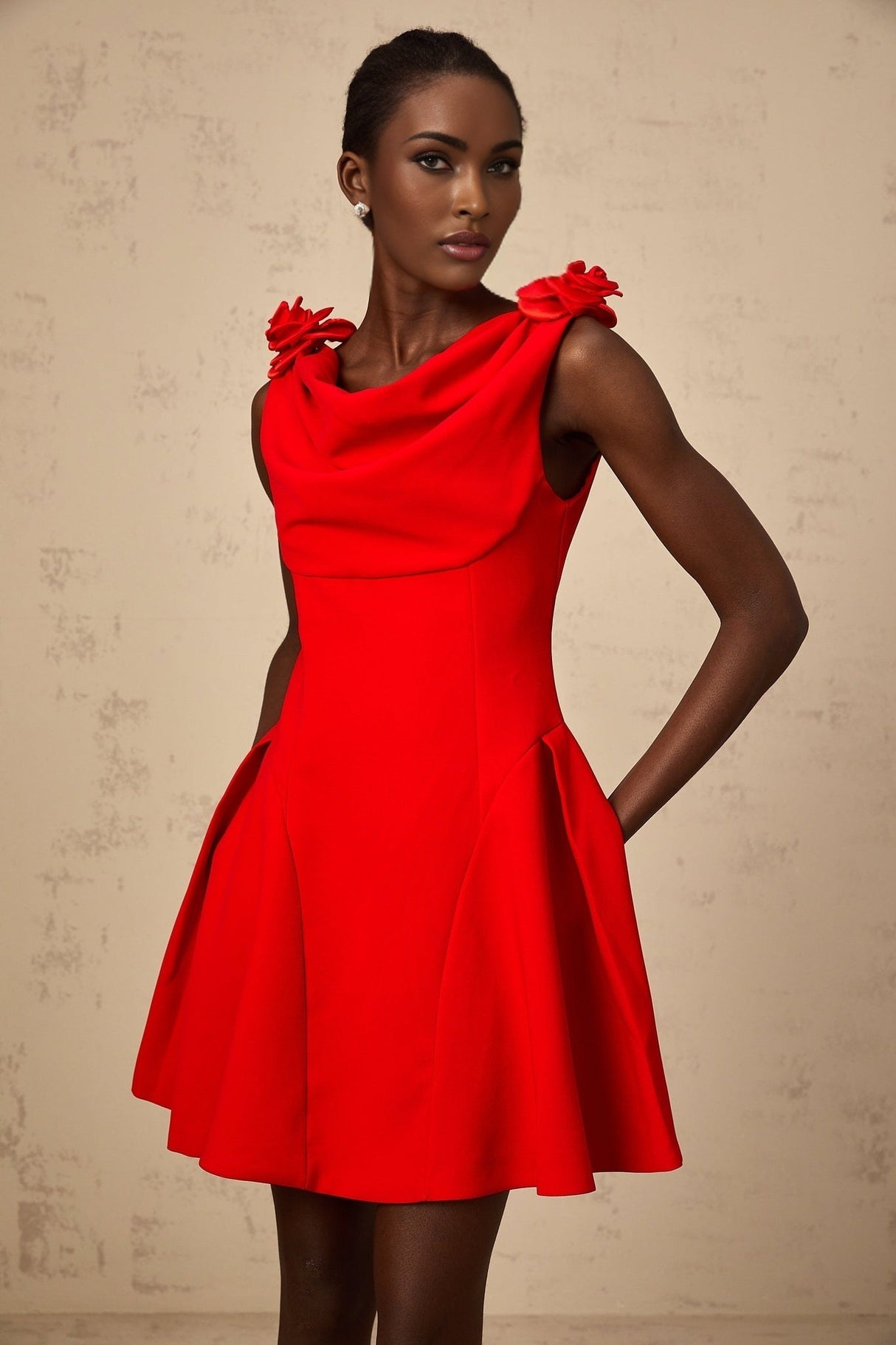 A red sleeveless mini dress with faux flower details worn by a model standing against a plain background