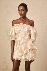 A short beige dress with an asymmetric design featuring a ruffled flounce detail and a mini length skirt