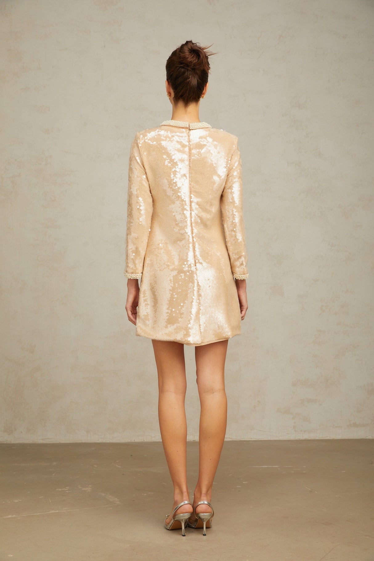 A short beige mini dress adorned with faux pearls and sequins creating a shimmering neutral toned look