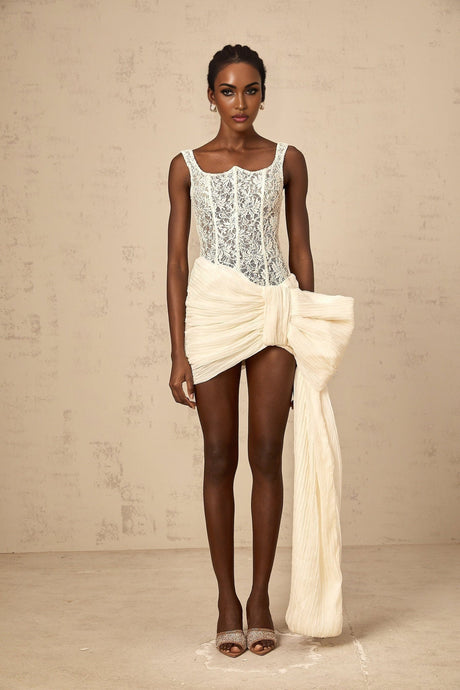 A short beige mini dress with a floral lace pattern and a bow detail at the waist