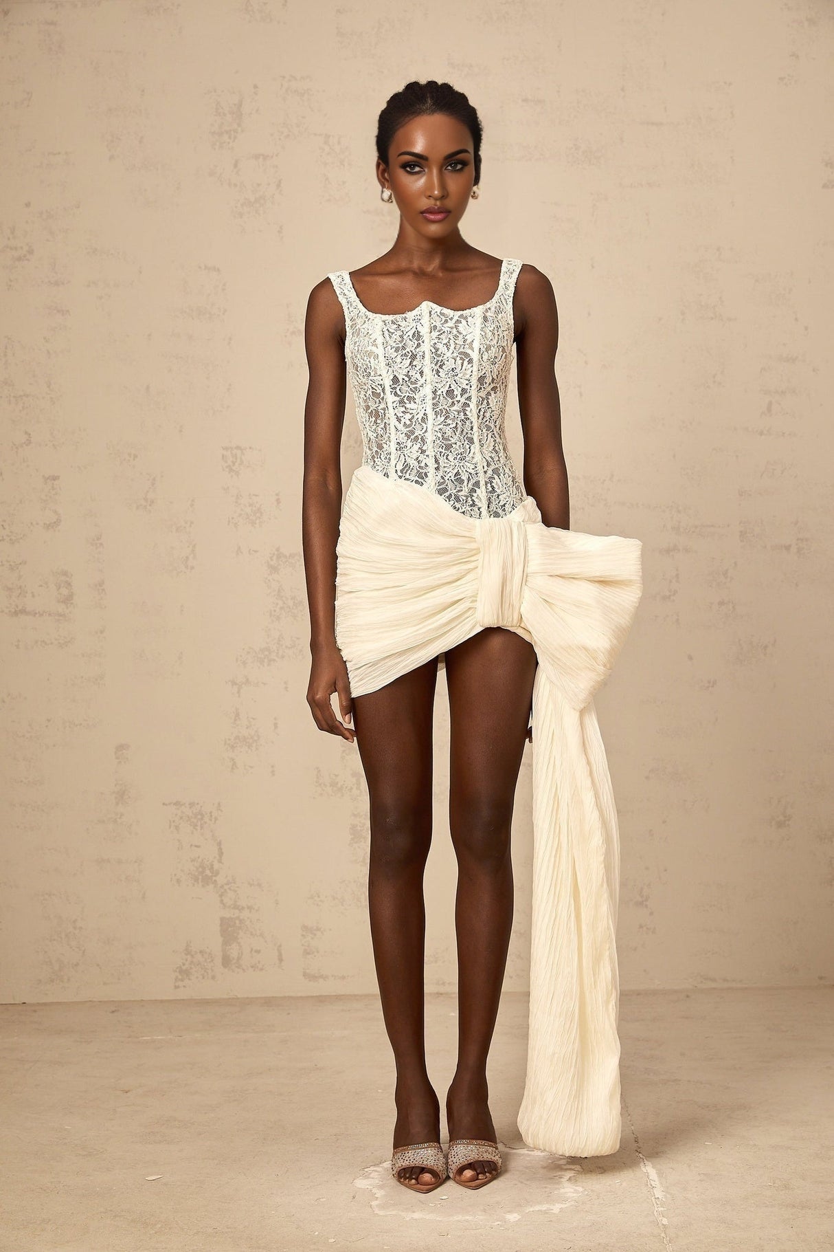 A short beige mini dress with a floral lace pattern and a bow detail at the waist