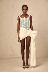 A short beige mini dress with a floral lace pattern and a bow detail at the waist