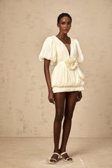 A short beige mini dress with pleated details and delicate floral appliques scattered across the fabric