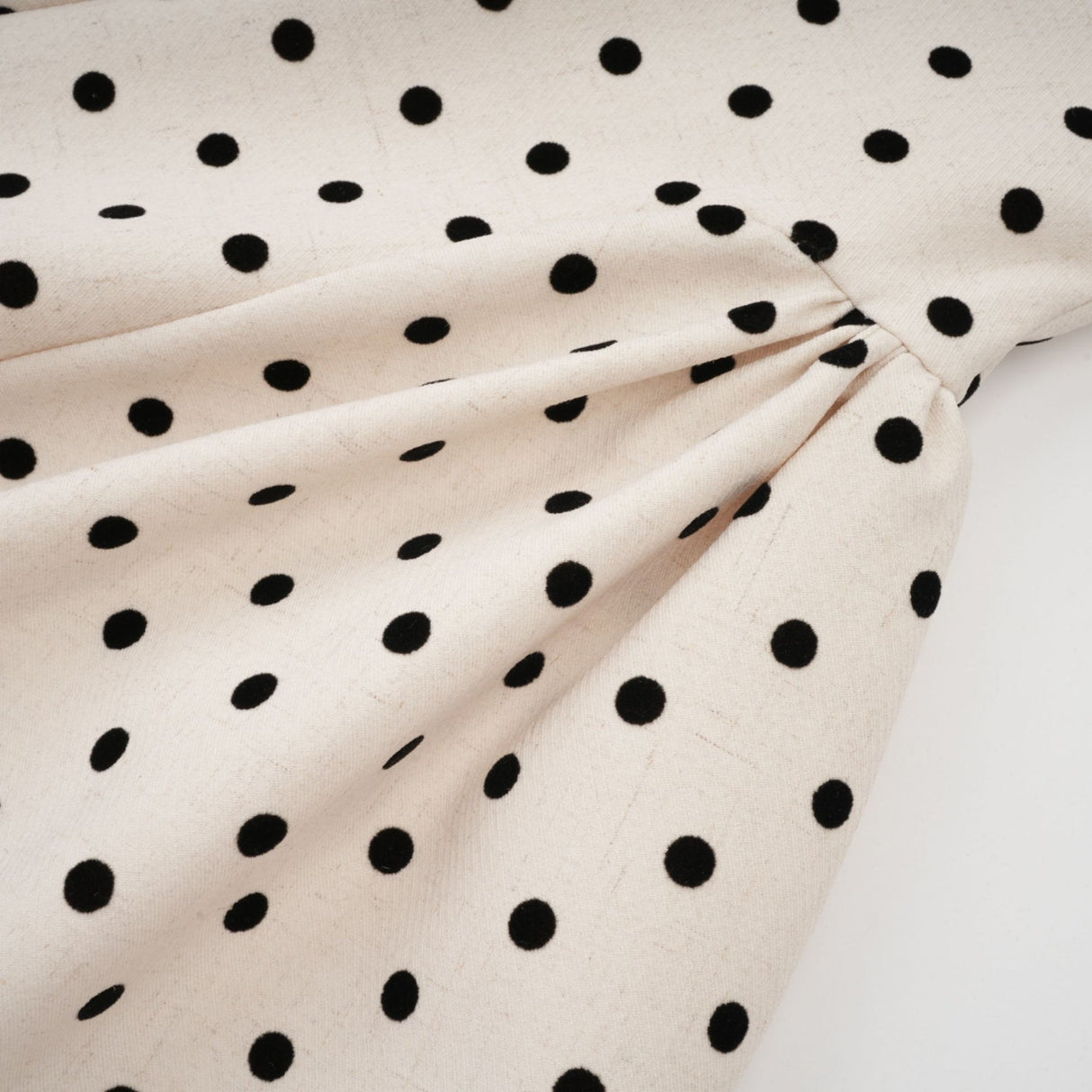 A short beige mini dress with polka dots and puff sleeves on a model against a neutral background