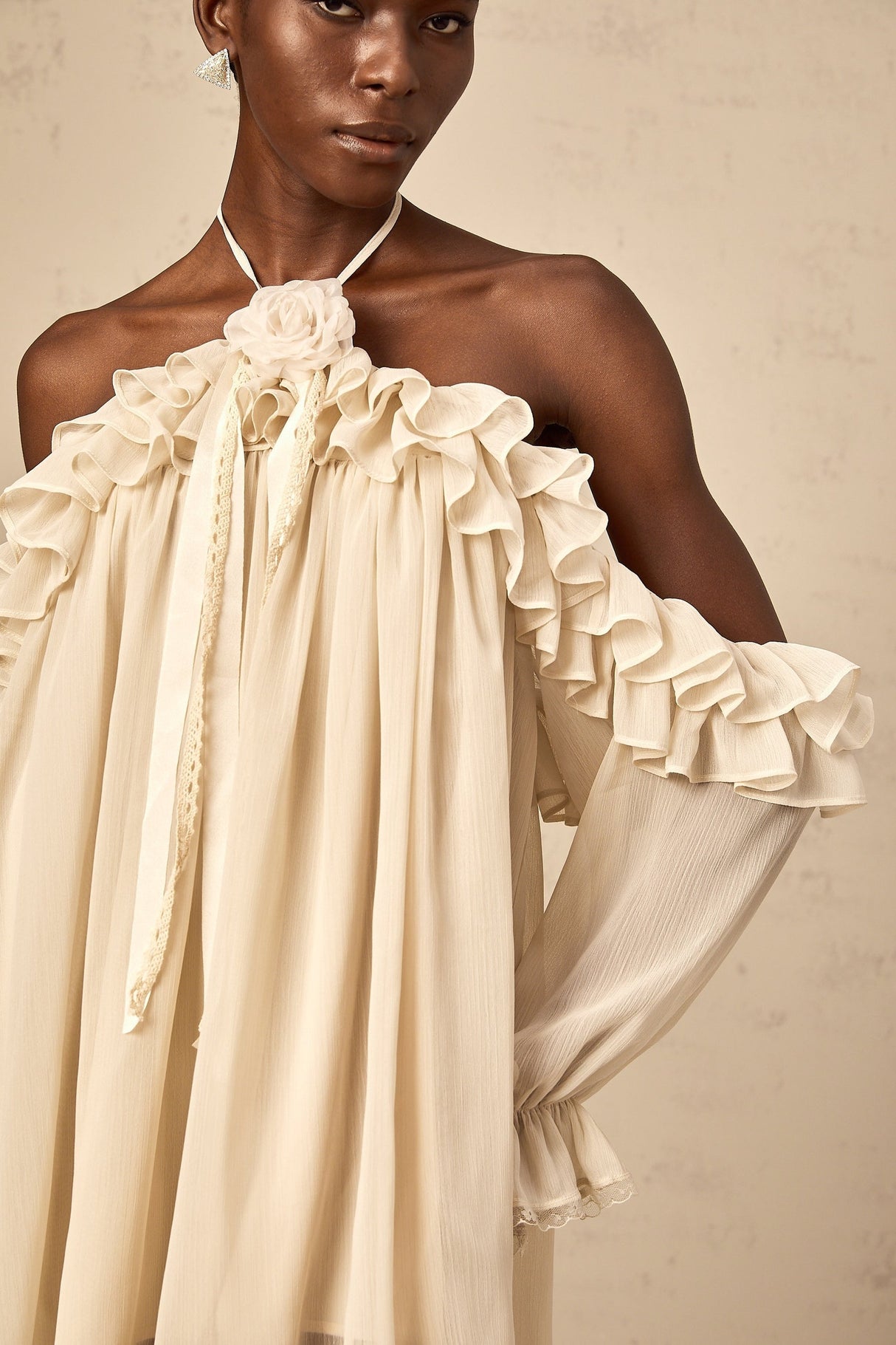 A short beige mini dress with ruffled details and delicate floral appliques scattered across the fabric creating a romantic and feminine look