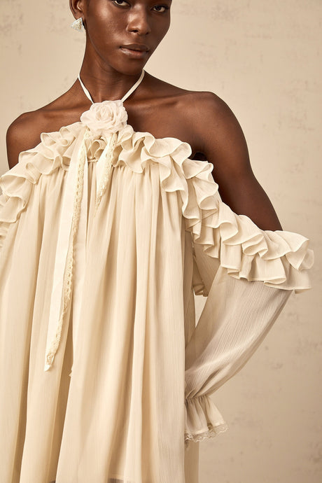 A short beige mini dress with ruffled details and delicate floral appliques scattered across the fabric creating a romantic and feminine look