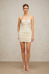 A short beige mini dress with small white polka dots featuring ruched detailing and a fitted silhouette