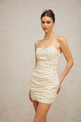 A short beige mini dress with small white polka dots featuring ruched details and a fitted silhouette
