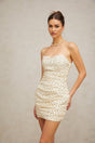 A short beige mini dress with small white polka dots featuring ruched details and a fitted silhouette