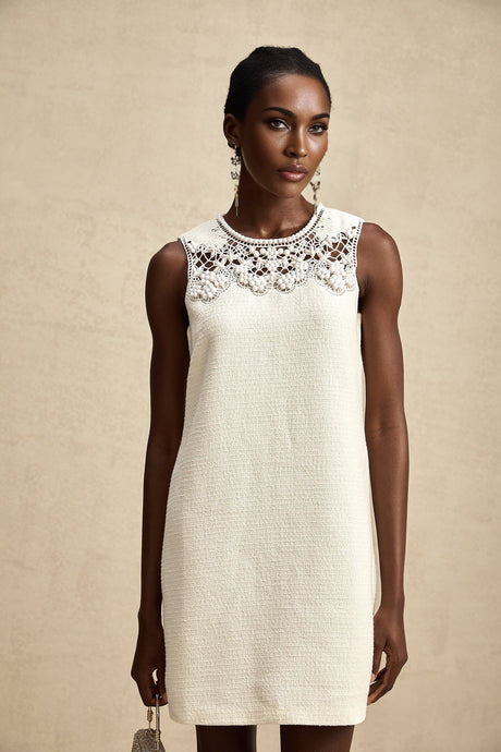 A short beige tweed mini dress with embroidered details and cutout sections worn by a model standing against a plain background