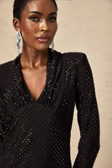 A short black mini dress with a deep plunging V neckline adorned with silver studs and embellishments featuring long sleeves and a figure hugging silhouette