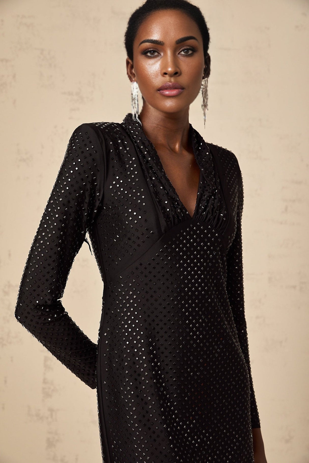 A short black mini dress with a plunging V neckline adorned with studded embellishments and featuring long sleeves
