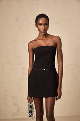 A short black mini dress with puffed sleeves and a prominent bow detail at the neckline