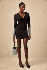 A short black mini dress with rhinestone embellishments and gathered fabric details worn by a model