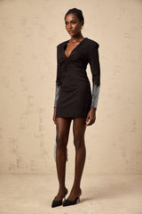 A short black mini dress with rhinestone embellishments and gathered fabric details worn by a model