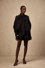 A short black mini dress with ruffled details and a pussybow neckline worn by a model