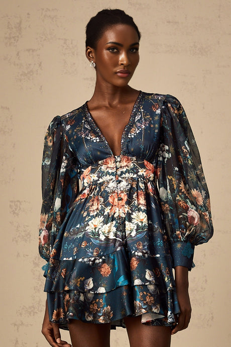 A short blue mini dress with a graphic print pattern and embellishments worn by a model standing against a plain background