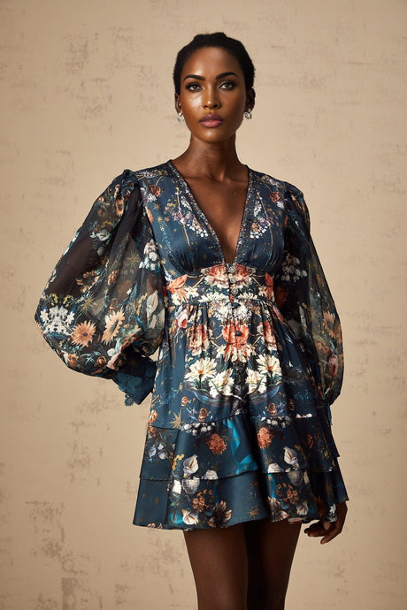 A short blue mini dress with graphic print design and embellishments worn by a model standing against a plain background