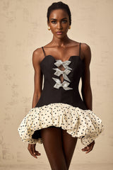 A short colorful mini dress with polka dot pattern and contrasting color blocks featuring a decorative bowknot detail
