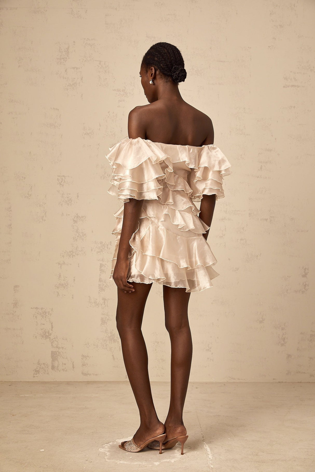 A short flouncy dress in neutral tones with an asymmetric design featuring ruffles and a cerise pink accent color