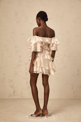 A short flouncy dress in neutral tones with an asymmetric design featuring ruffles and a cerise pink accent color