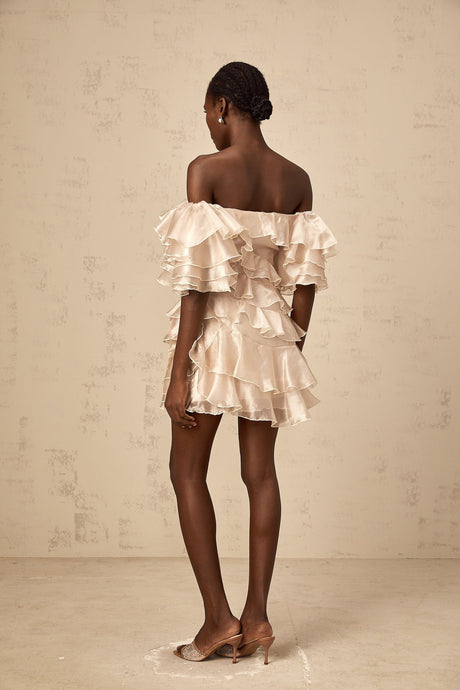 A short flouncy dress in neutral tones with an asymmetric design featuring ruffles and a cerise pink accent color