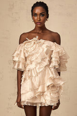 A short neutral colored dress with an asymmetric design featuring a flounce detail and a mini length
