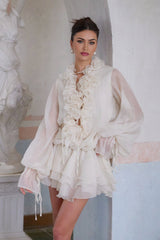 A short neutral colored dress with tiered layers and floral applique details featuring a mini length and delicate design