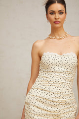 A short neutral colored mini dress with polka dot pattern and ruched detailing