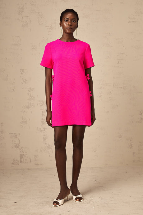 A short pink mini dress with a bow detail likely featuring a feminine and playful design suitable for dressy occasions