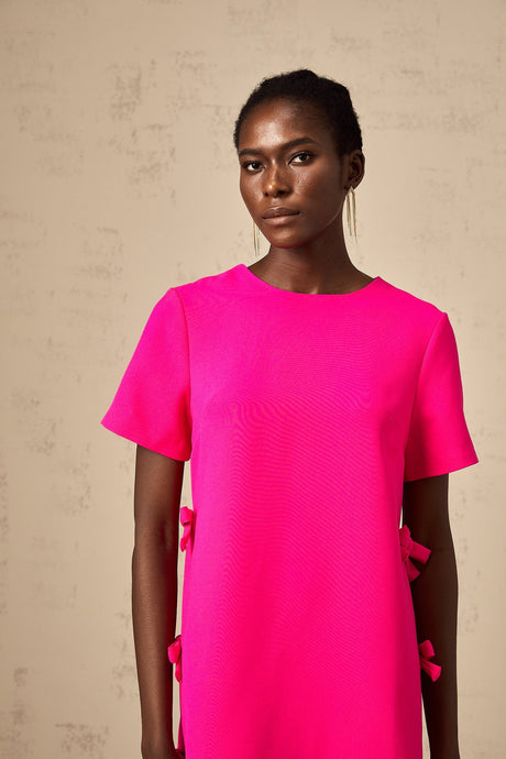 A short pink mini dress with a prominent bow detail likely featuring a feminine and playful design suitable for dressy occasions