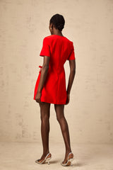 A short red mini dress with short sleeves and a bow detail worn by a model against a plain background