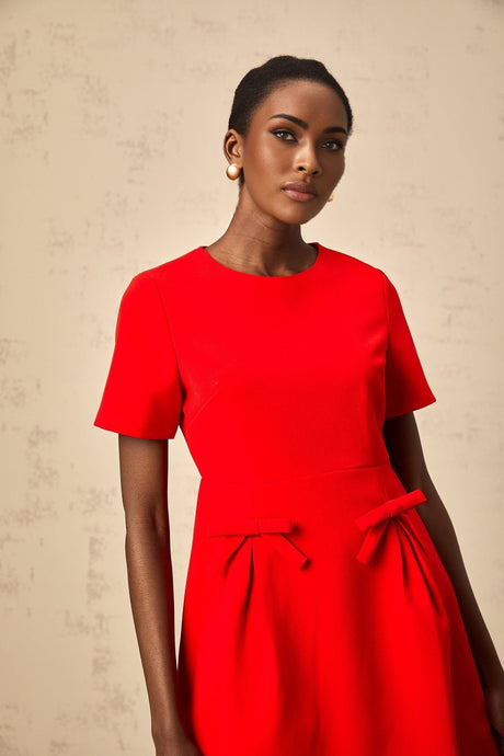 A short red mini dress with short sleeves and a bow detail worn by a model against a plain background