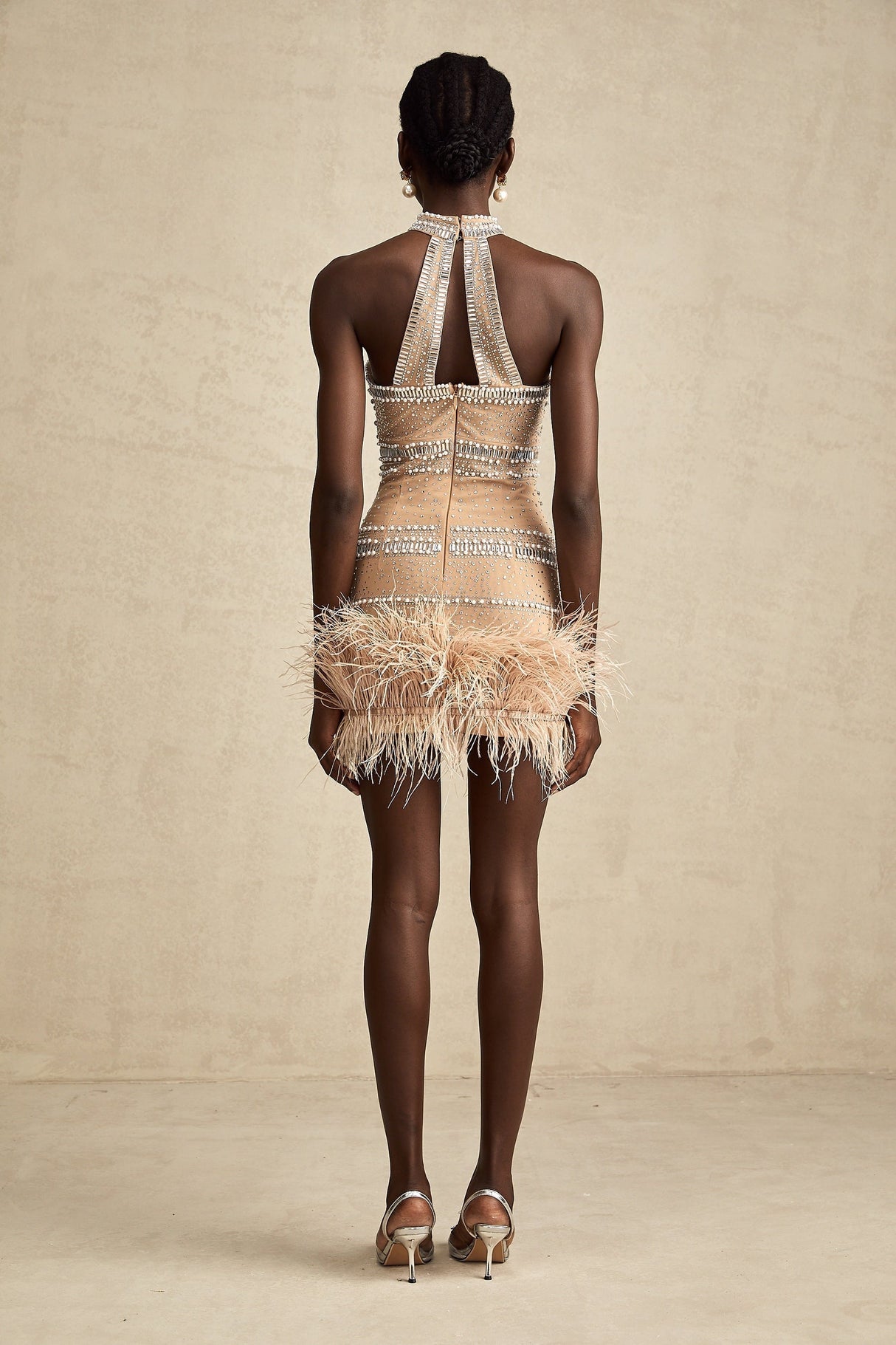 A short sleeveless mini dress with crystal embellishments and feather trim along the hemline