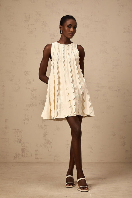 A short sleeveless white mini dress with wavy details along the edges named Axelle