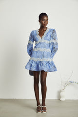 A short white dress with floral embroidery and a Vneckline on a model against a plain background