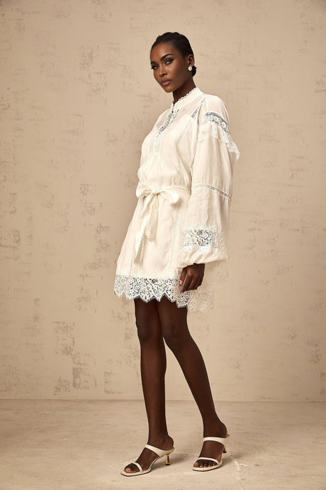 A short white dress with floral lace trim details and a mini length skirt
