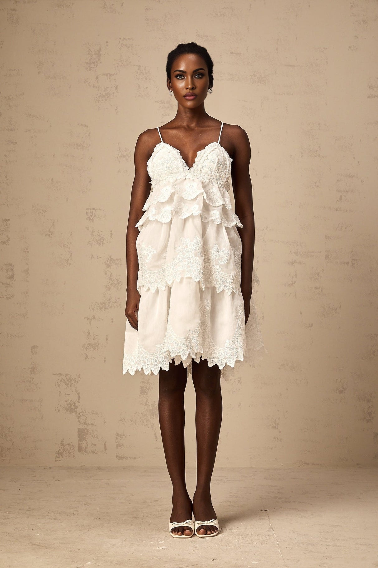 A short white dress with tiered layers made of intricate guipure lace featuring a mini length and delicate floral patterns throughout the fabric