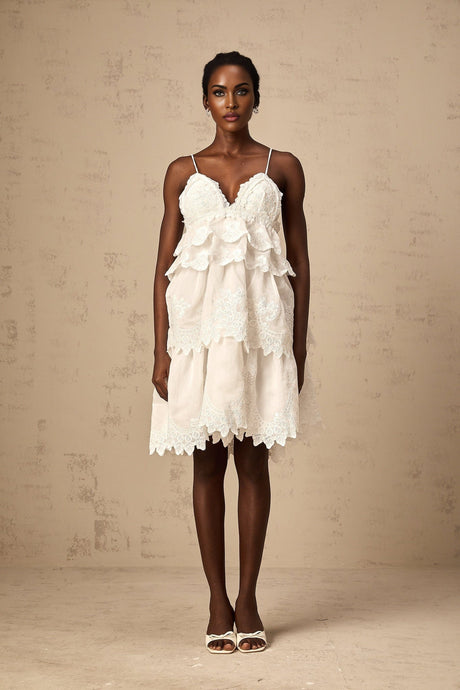 A short white dress with tiered layers made of intricate guipure lace featuring a mini length and delicate floral patterns throughout the fabric