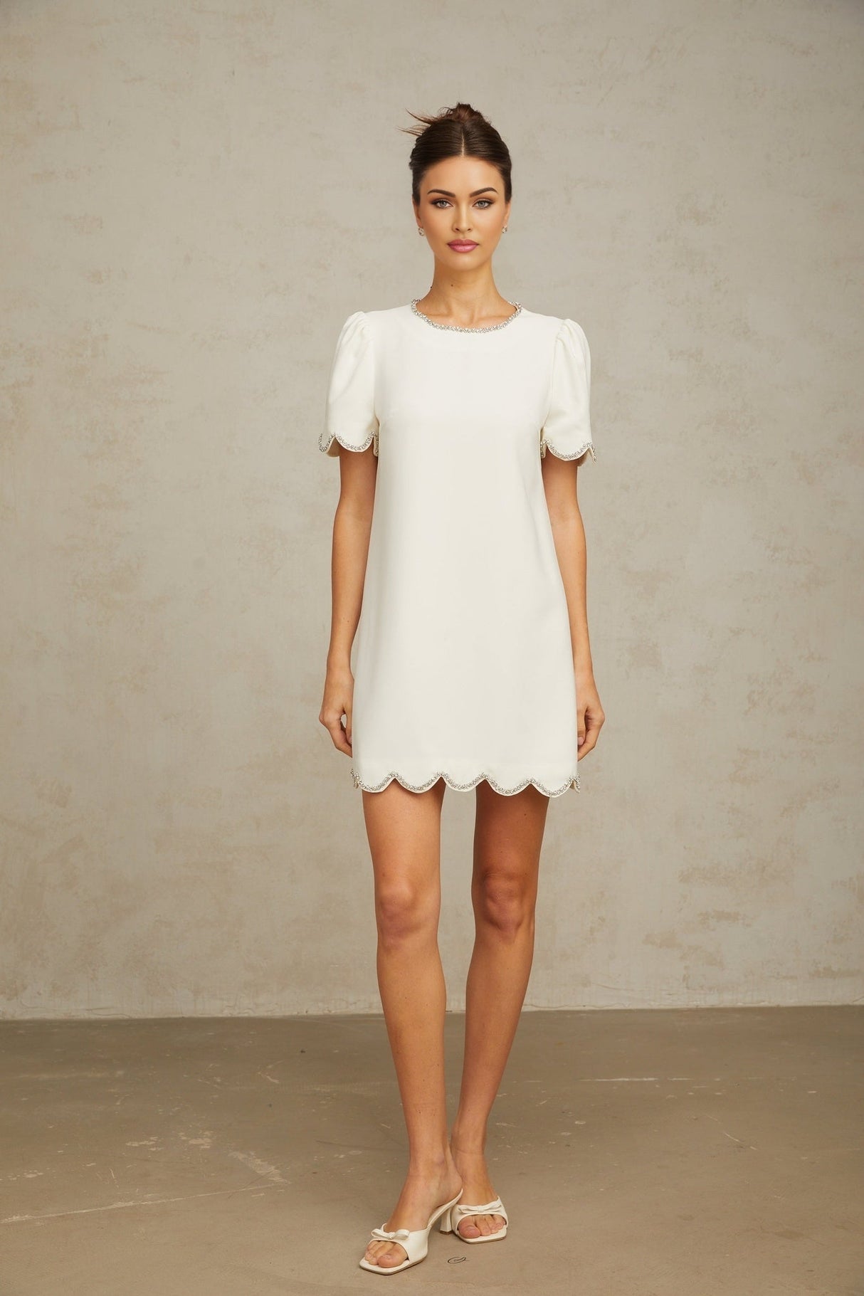 A short white mini dress adorned with crystal embellishments featuring a fitted silhouette and delicate detailing
