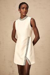 A short white mini dress adorned with crystal embellishments featuring a simple silhouette and sleeveless design