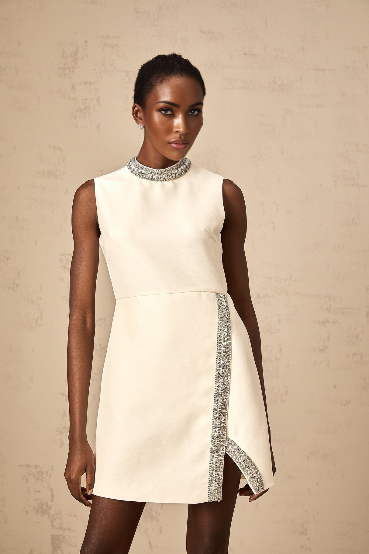 A short white mini dress adorned with sparkling crystal embellishments featuring a fitted silhouette and delicate details