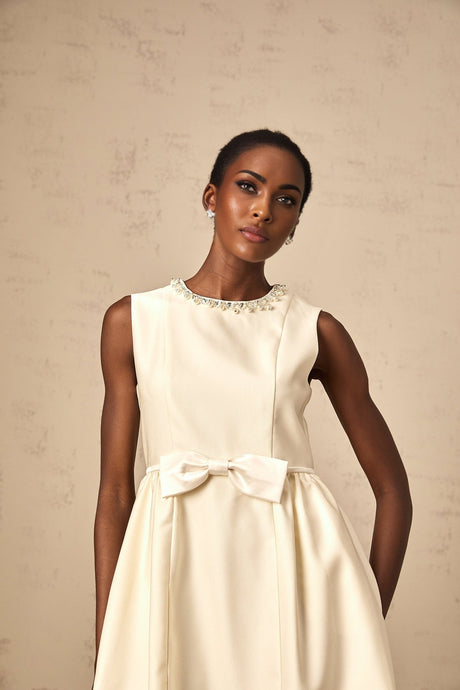A short white mini dress with a bow accent featuring a fitted silhouette and named Isabelle